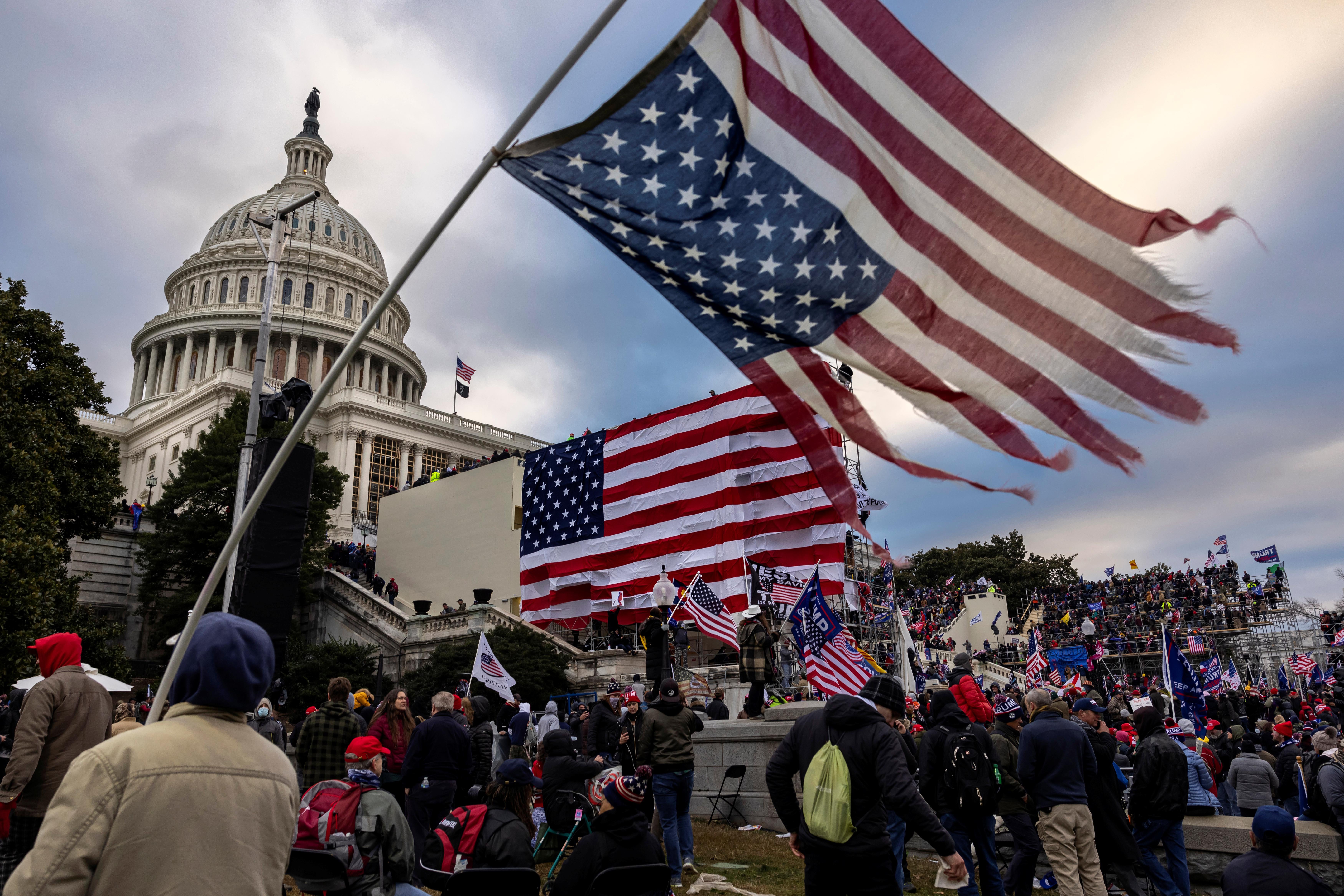 A frayed upside-down American flag flies in front of Trump supporters massed on the Capitol steps.