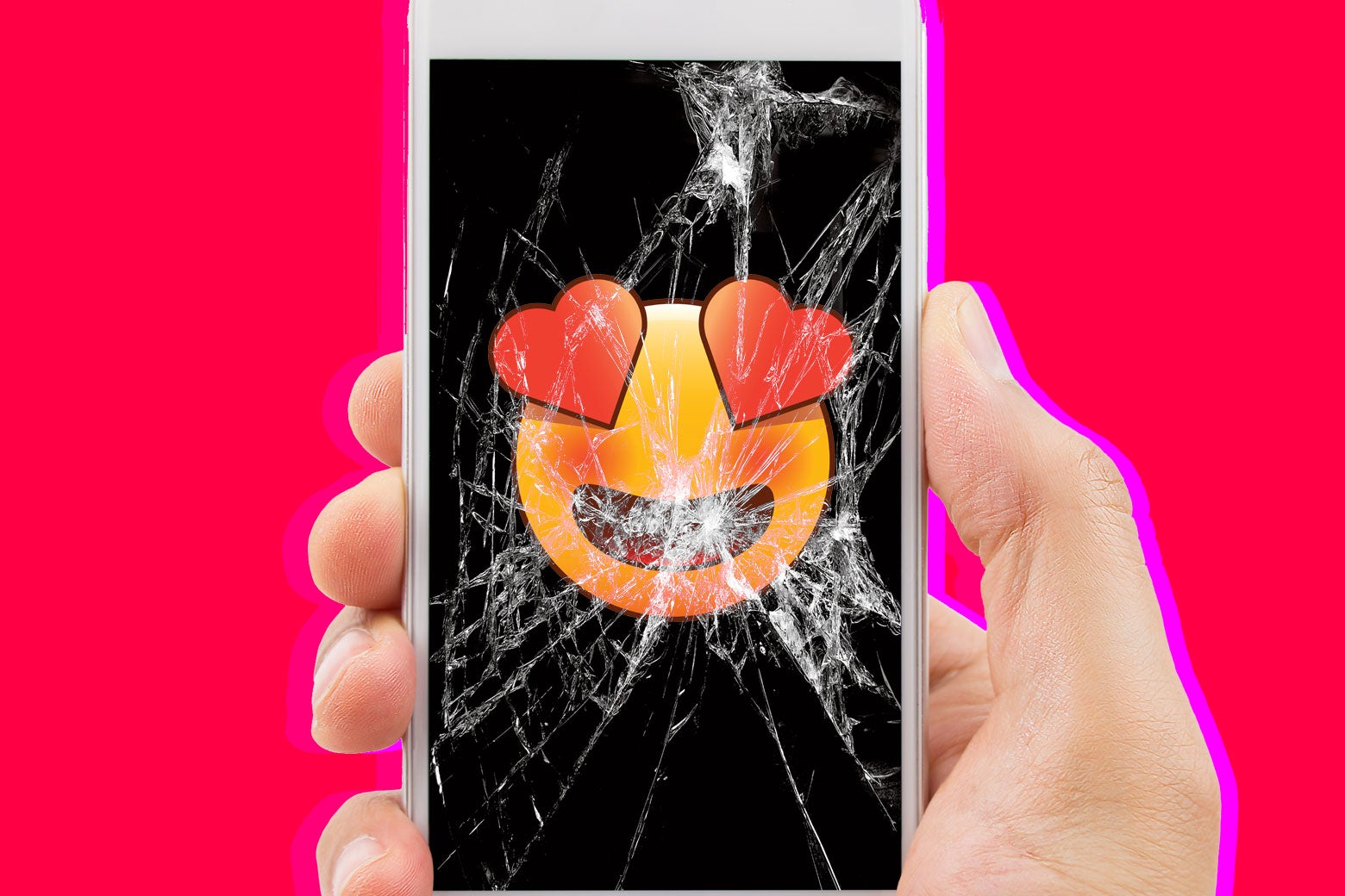 Photo illustration: A heart-eyes emoji is shown on the screen of a severely cracked phone in someone’s hand.