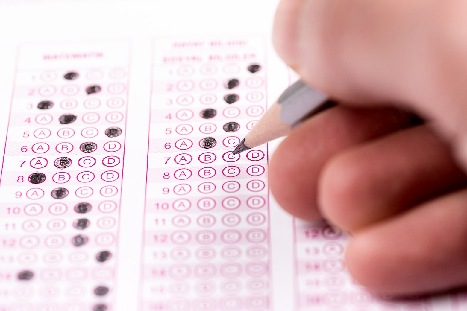A hand holding a pencil over a multiple choice test form on which some bubbles have already been filled in.
