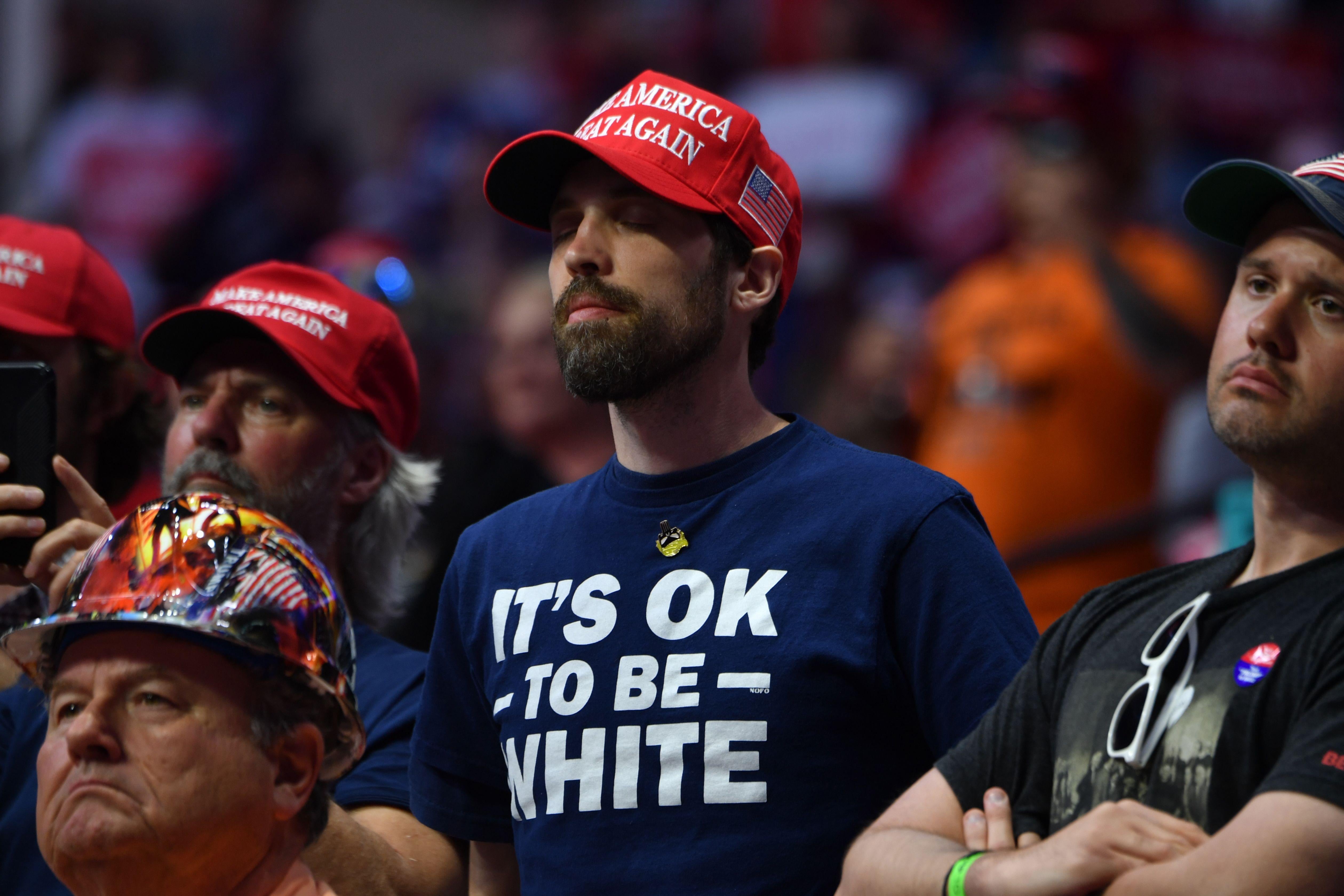 Man wearing an "It's OK to Be White" shirt in the audience of Trump supporters listening as Trump speaks