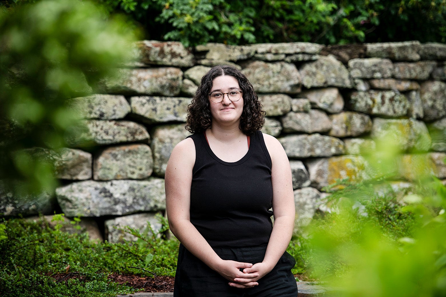 A young woman wearing all black stands in a garden.