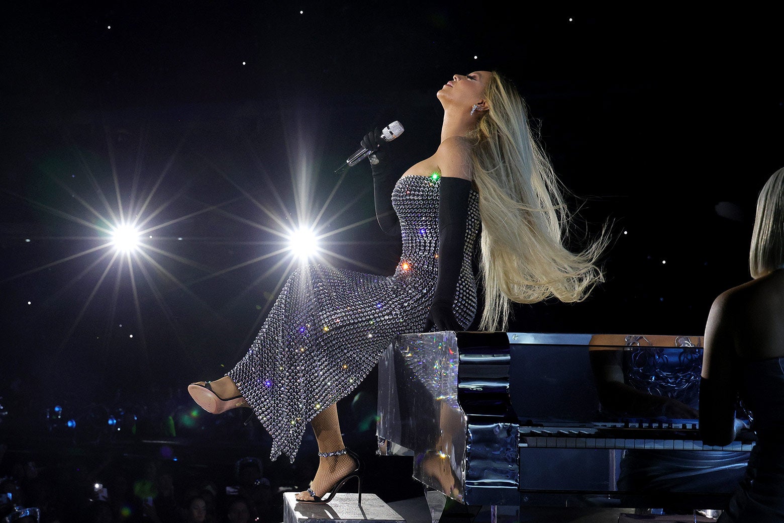 Beyoncé dressed in a glittery gown, sitting on a piano onstage.