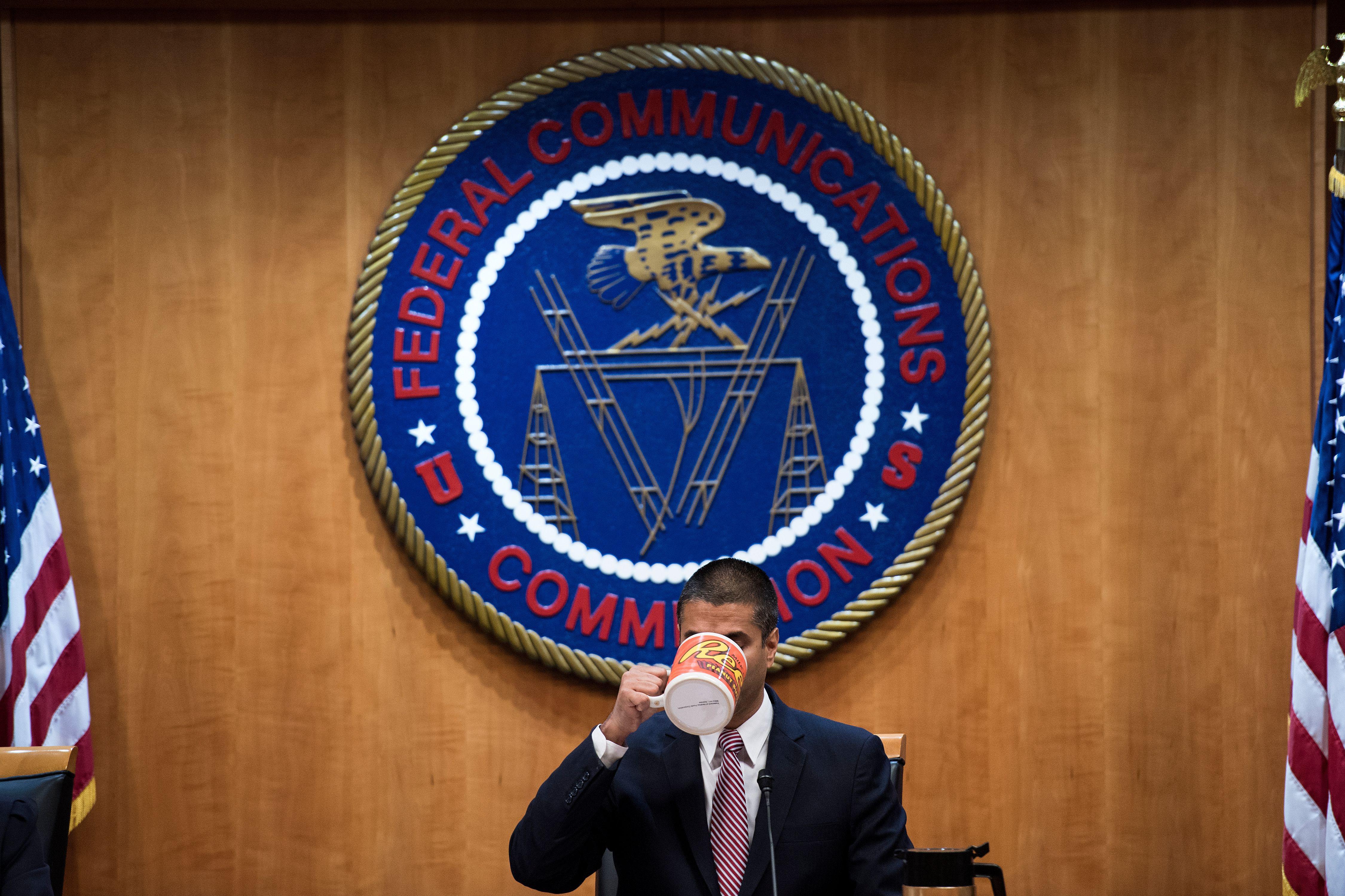 Ajit Pai sips from a giant Reese's mug beneath the seal of the FCC.