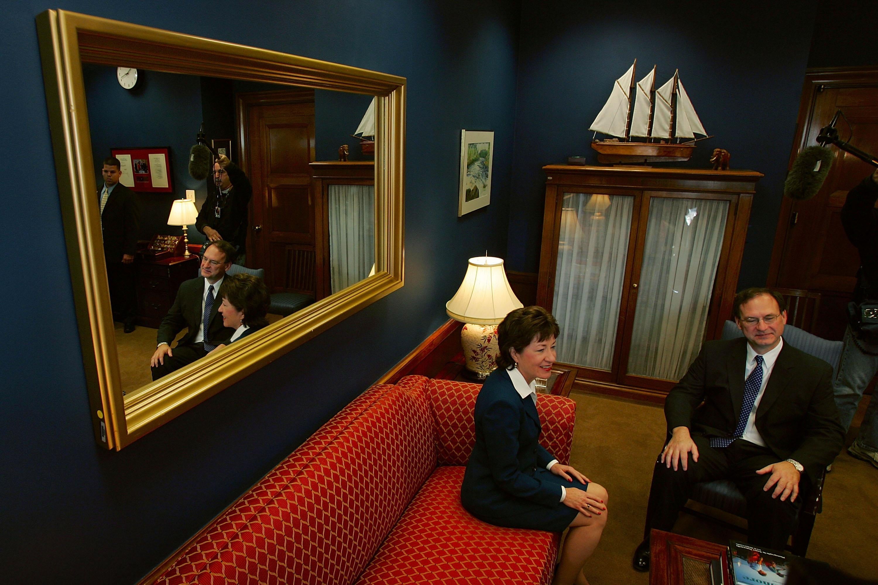 Alito sits in a chair next to Collins sitting on a red couch in a traditionally decorated Capitol room