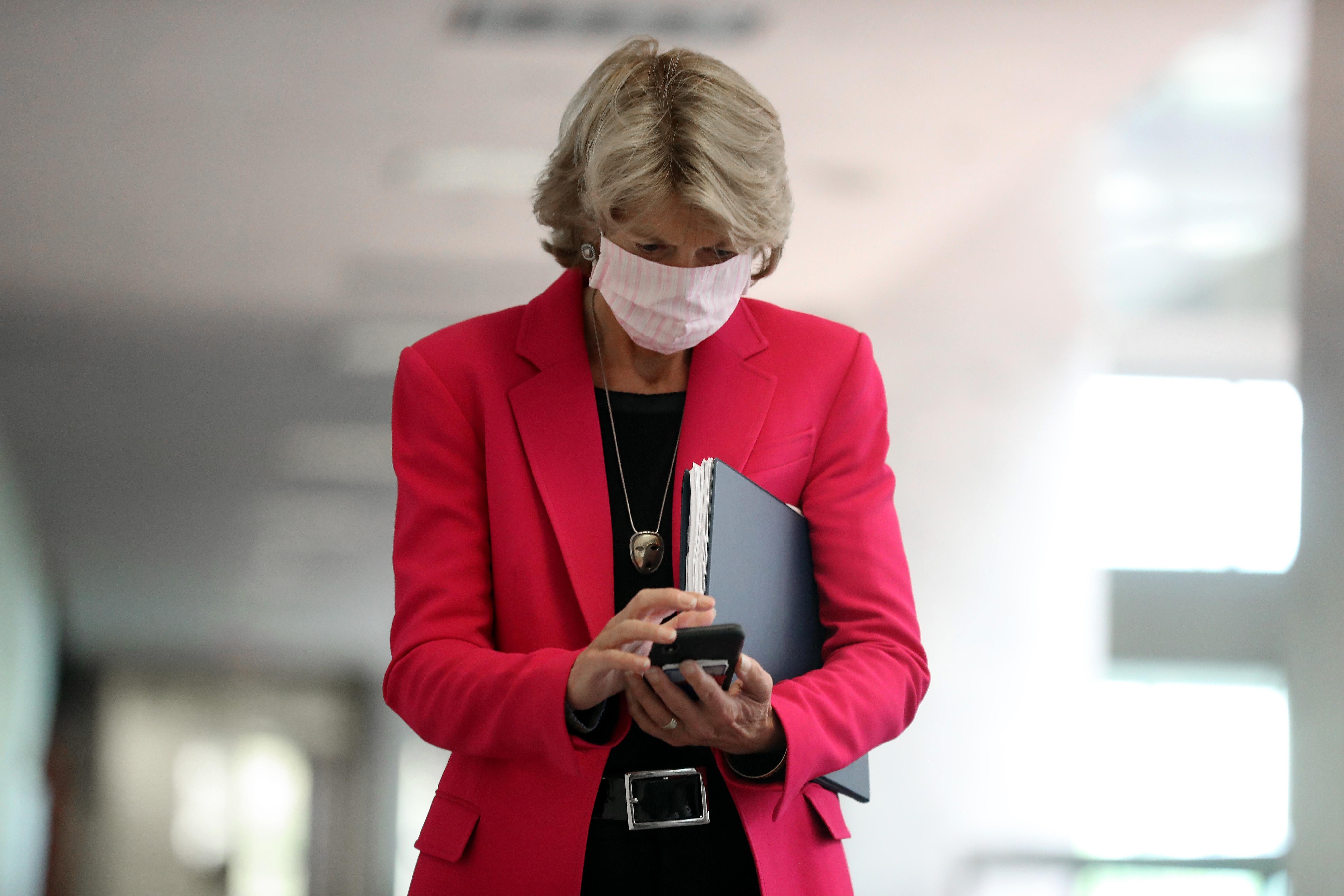 Lisa Murkowski, wearing a pink suit, looks down at her phone.