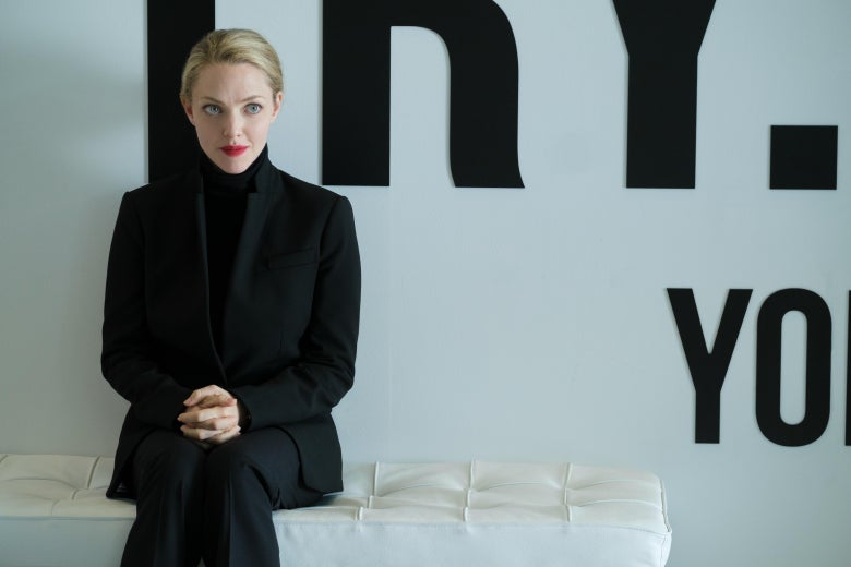 Amanda Seyfried in The Dropout, in a black suit in front of a white wall with lettering.