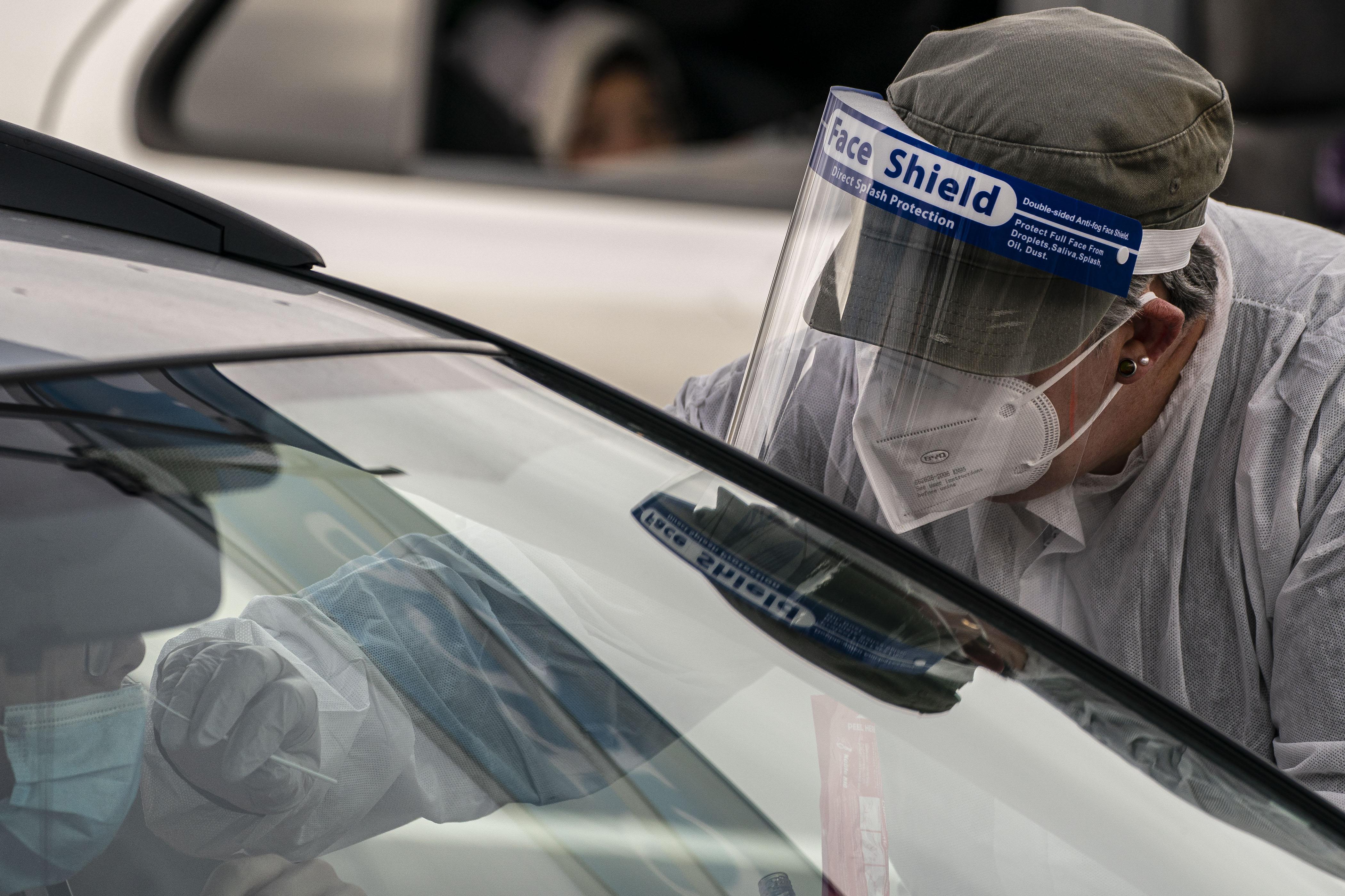 A nurse wearing full PPE administers a Covid-19 test through a car window. 