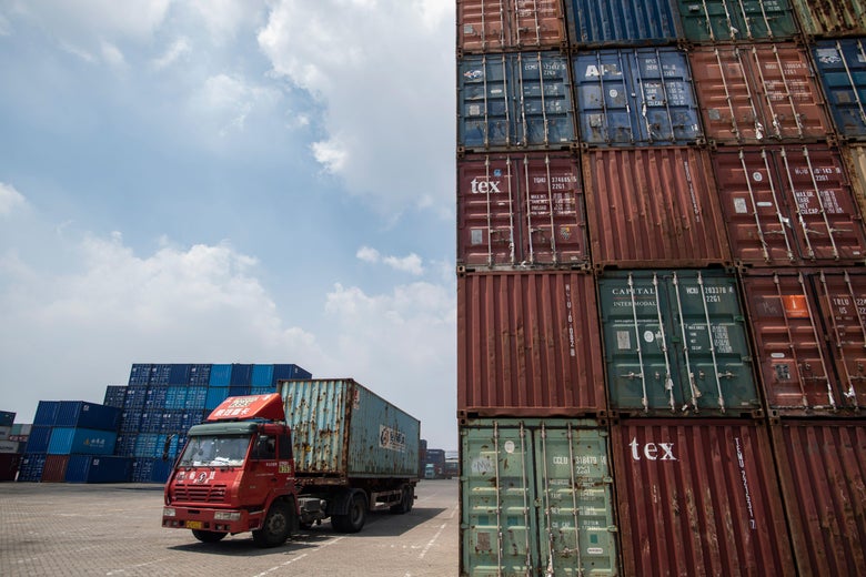 A truck transports a container next to stacked containers at a port in China.