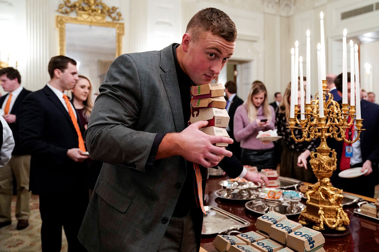 A Clemson player carries fast-food hamburgers provided by President Trump due to the partial government shutdown on Monday. It's a stack of several seemingly burger-size take-out boxes from McDonald's, and they're tucked under his chin and cradled in his hands.