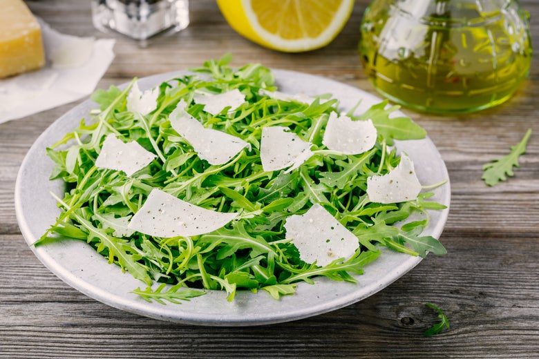 A bowl of arugula with parmesan shavings.