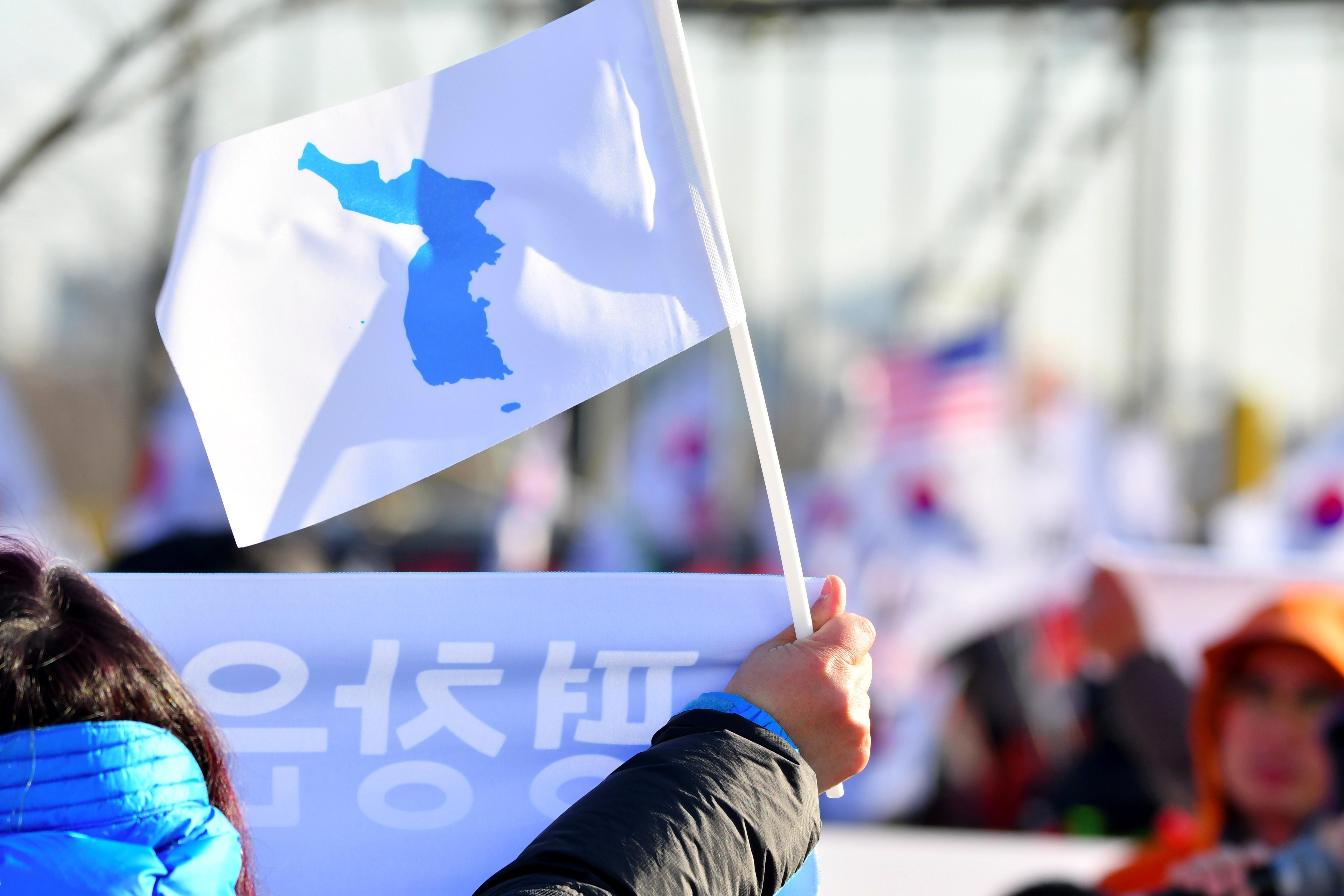 A South Korean supporter of the unified Korea female ice hockey team wave a 'Unification flag' toward people protesting against the team, outside an ice rink before a friendly ice hockey match between the combined team and Sweden, in the western city of Incheon on February 4, 2018 ahead of the Pyeongchang 2018 Winter Olympic Games. / AFP PHOTO / KIM DOO-HO        (Photo credit should read KIM DOO-HO/AFP/Getty Images)