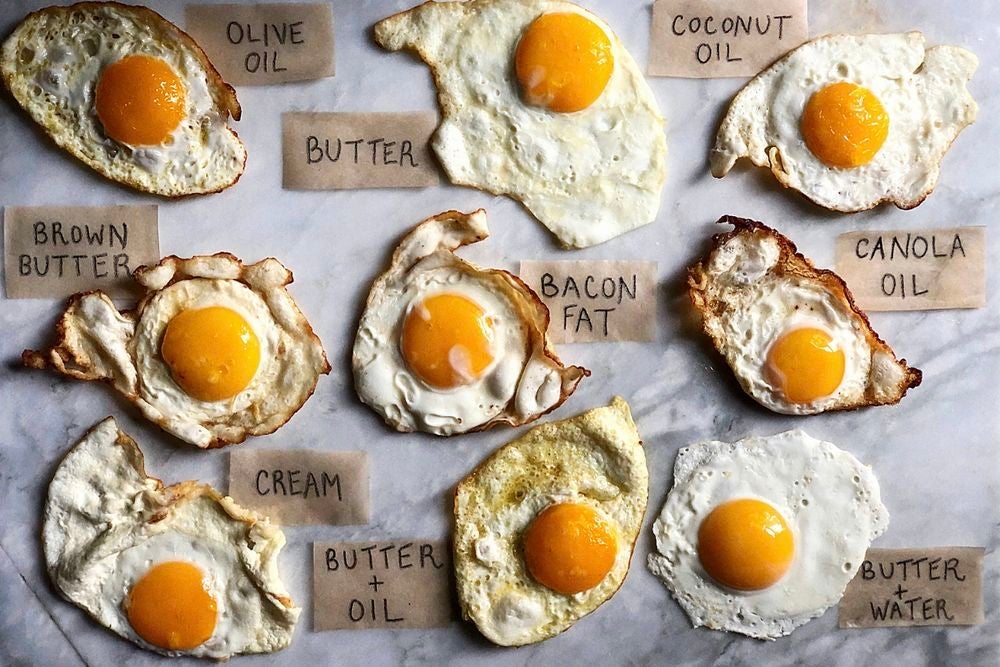 Nine fried eggs labeled with frying method. Clockwise from top left: olive oil, butter, coconut oil, canola oil, butter + water, butter + oil, cream, brown butter, bacon fat.