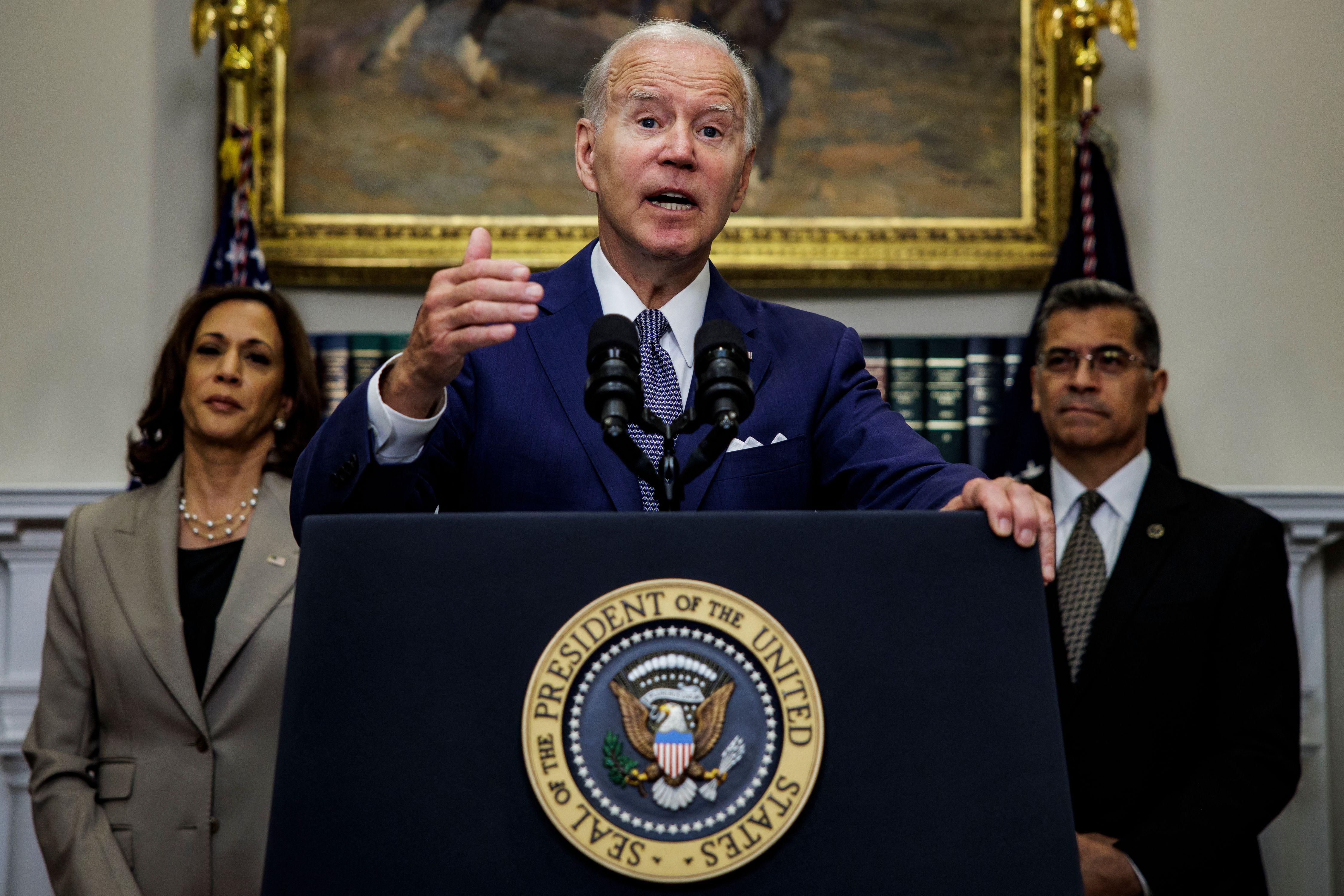 Joe Biden gestures while speaking at a podium next to Harris and Becerra.