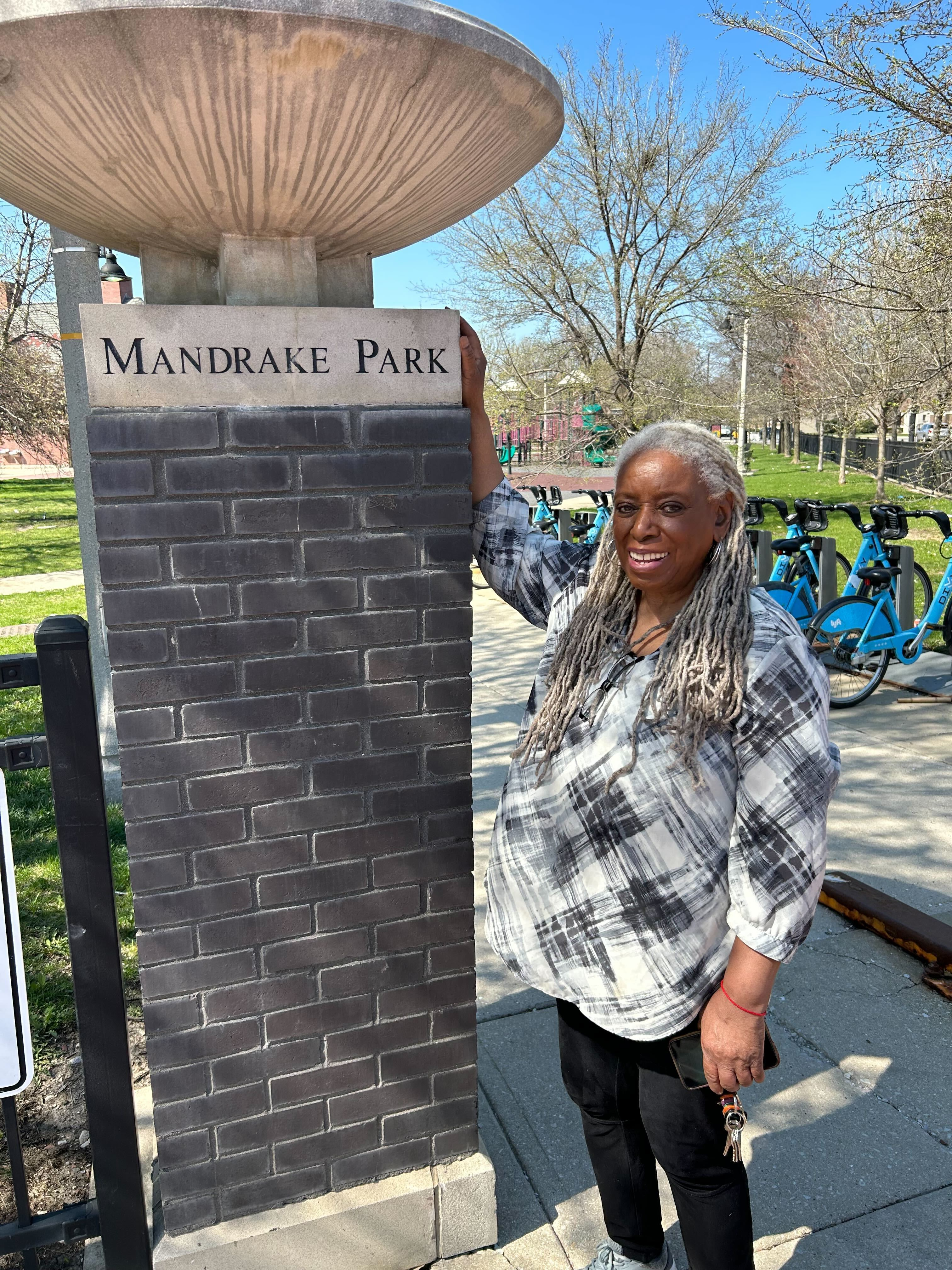 A woman with silver hair standing next to a column that reads "Mandrake Park."
