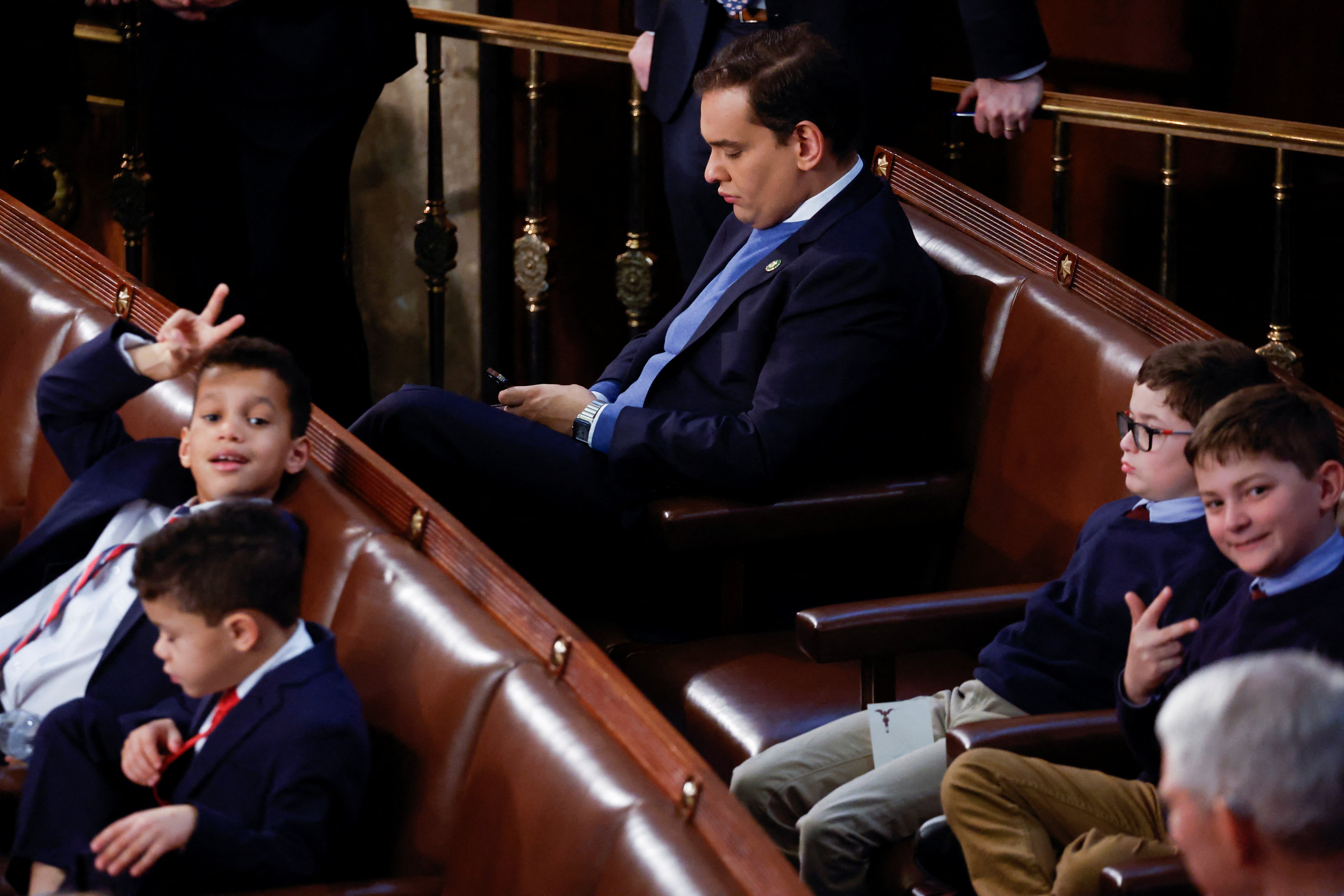 George Santos, an incoming House rep. from New York who lied about nearly every aspect of his background and biography, looking at his phone, sitting near kids, in Congress.