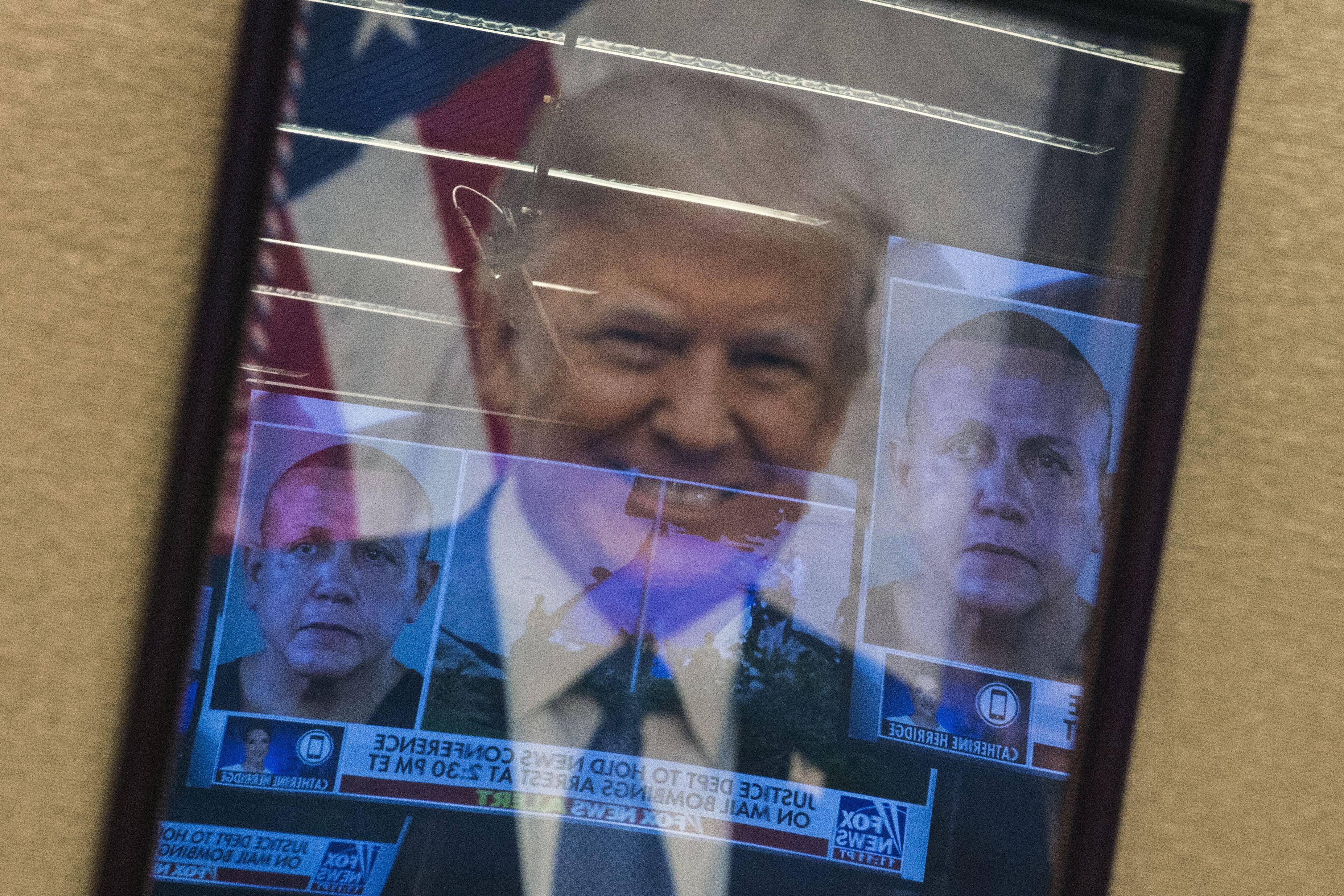 Mugshots of bombing suspect Cesar Sayoc are reflected on a portrait of U.S. President Donald Trump prior to a press conference at the Department of Justice in Washington, DC on October 26, 2018.