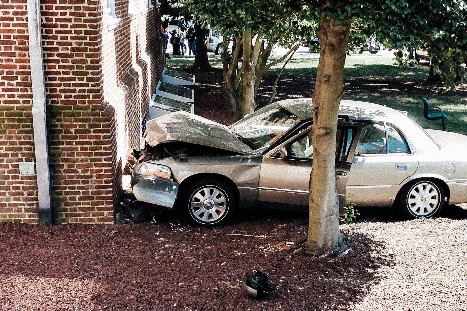 A car crashed into a brick wall, with its front crunched up from the collision. 