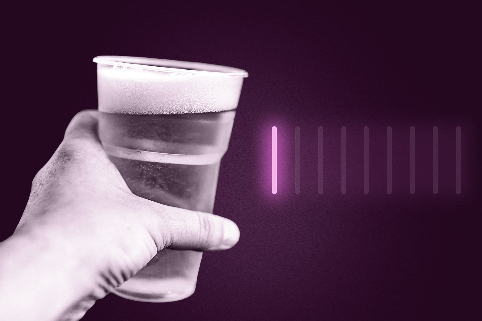 A man's hand holds a clear plastic cup of beer. 