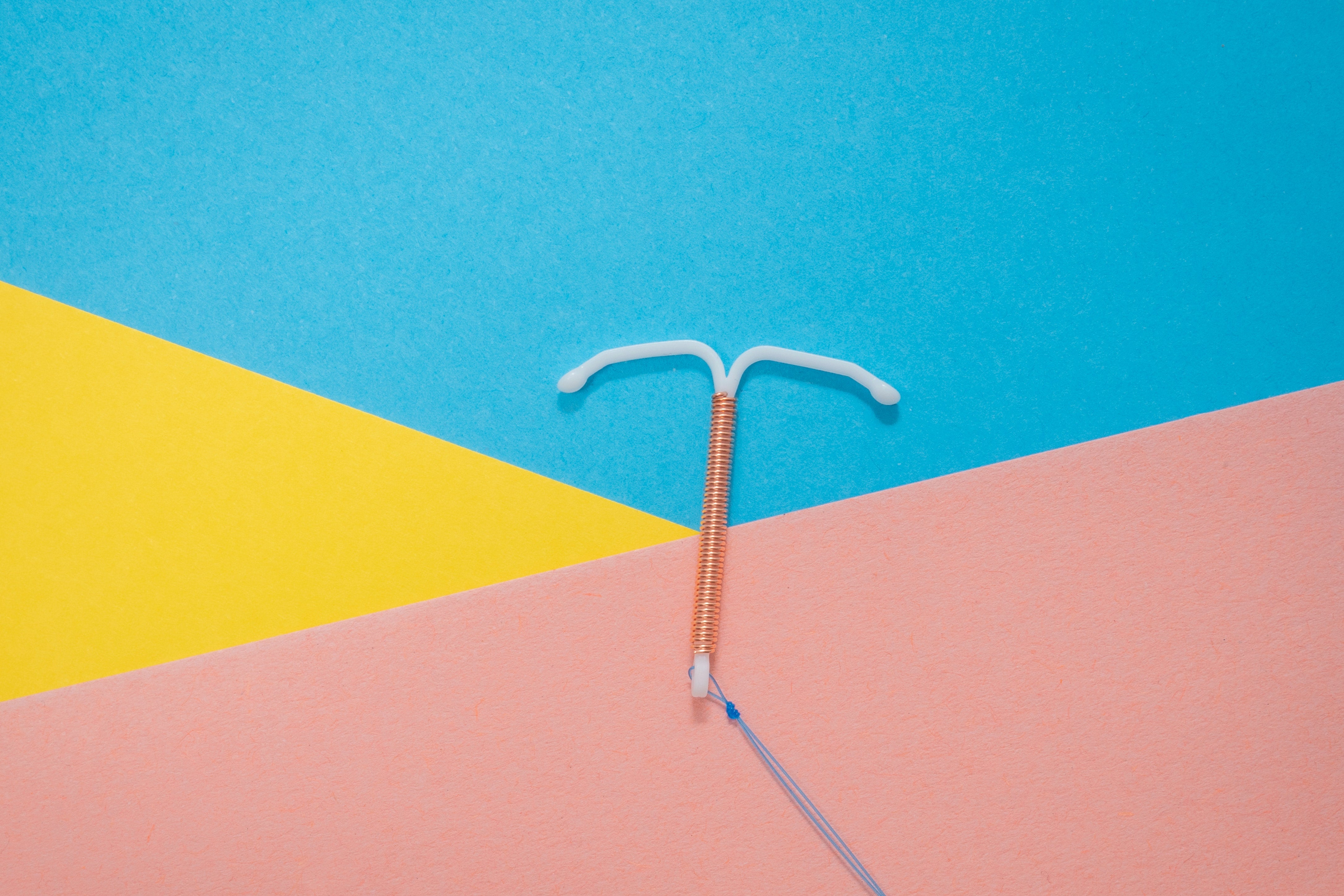An IUD on a pink, blue, and yellow background. The whole vibe is happy! 