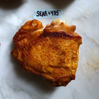 A cooked chicken thigh with golden brown skin labeled Sear + 475 degrees.