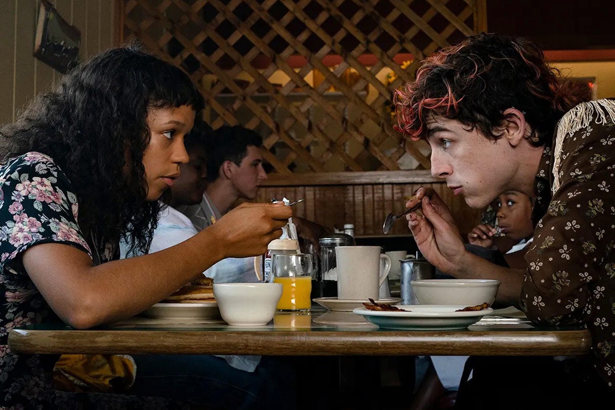 Taylor Russell and Timothée Chalamet sit across a table from each other at a restaurant. 