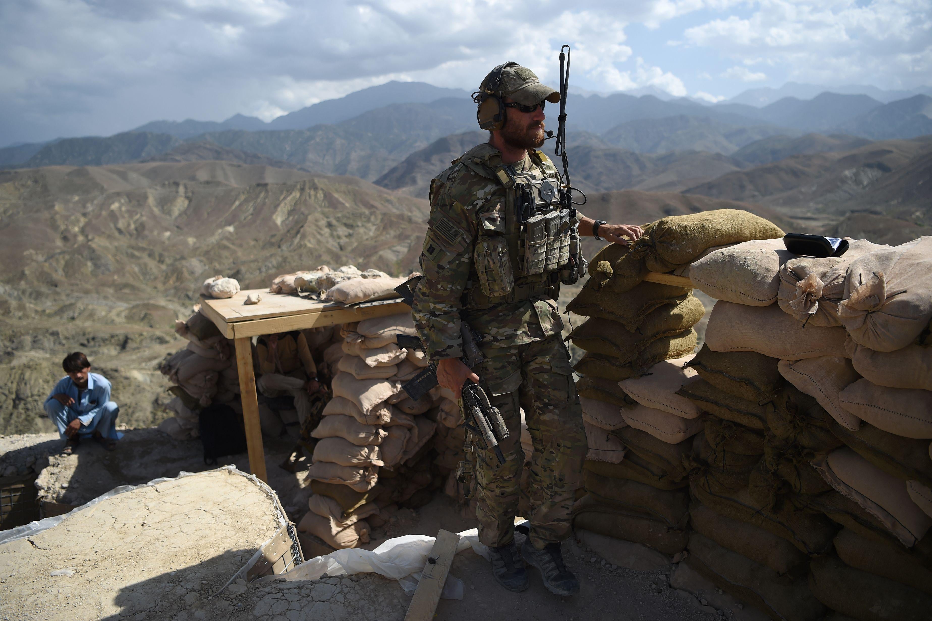 A soldier stands beside a sandbag barrier overlooking a hillside in Afghanistan.