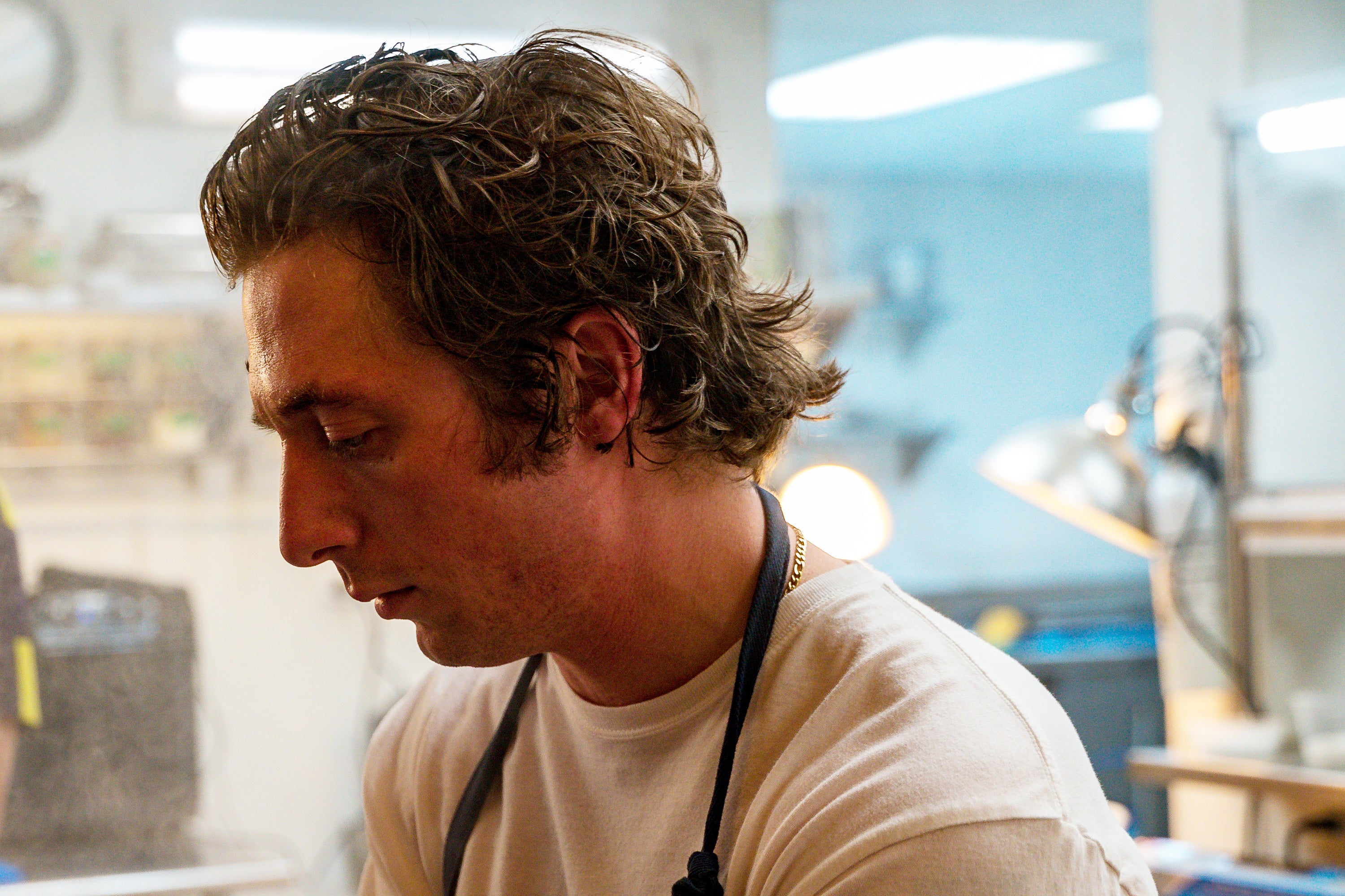 A very dreamy man with long, mussy hair in a restaurant kitchen.