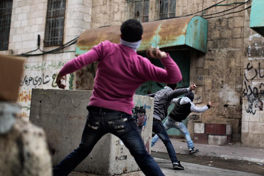 Palestinian demonstrators throw stones towards Israeli troops during clashes in the old city of Hebron on March 1, 2013 following a protest demanding the reopening of Shuhada Street, the one-time heart of the city, which has been declared off-limits to Palestinians and can only be used by Jewish settlers. 