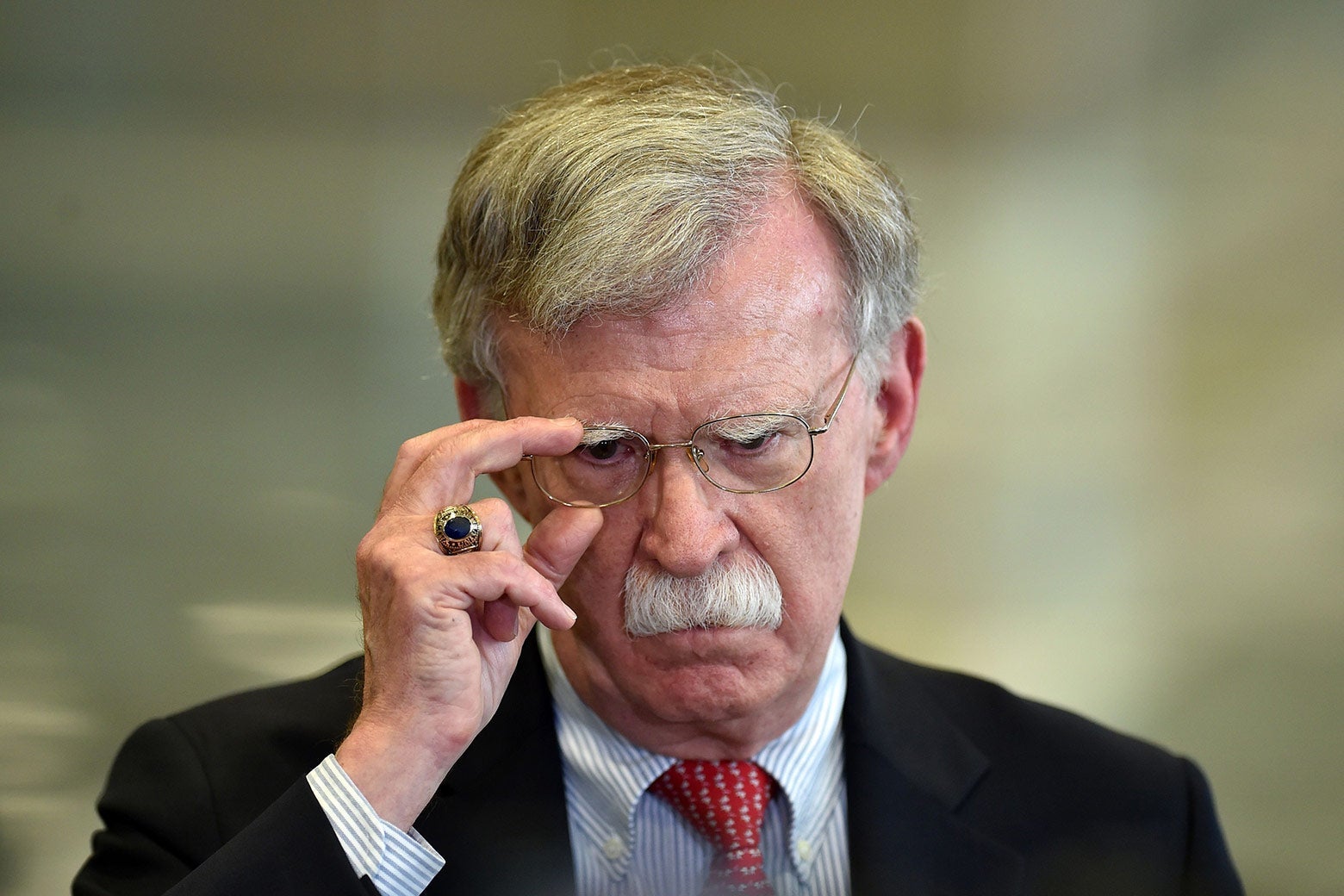 Bolton adjusts his glasses as he looks off-camera.