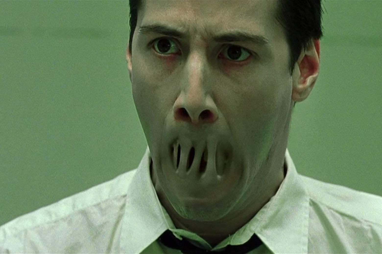 Keanu Reeves, in a still from the Matrix, staring in horror as his lips seal together.