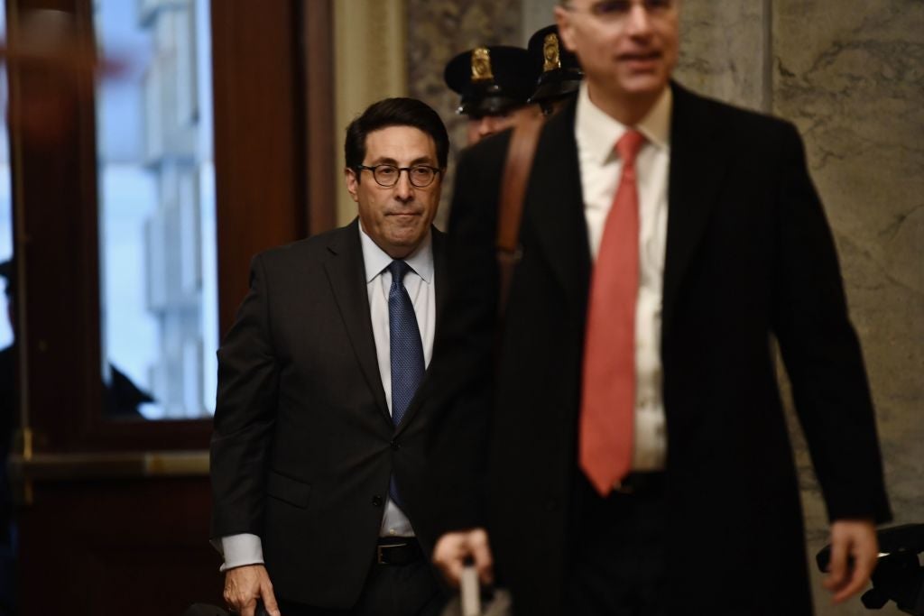 Sekulow, wearing a dark suit and holding a briefcase, walks behind another attorney and past two law enforcement officers in a marble hallway.