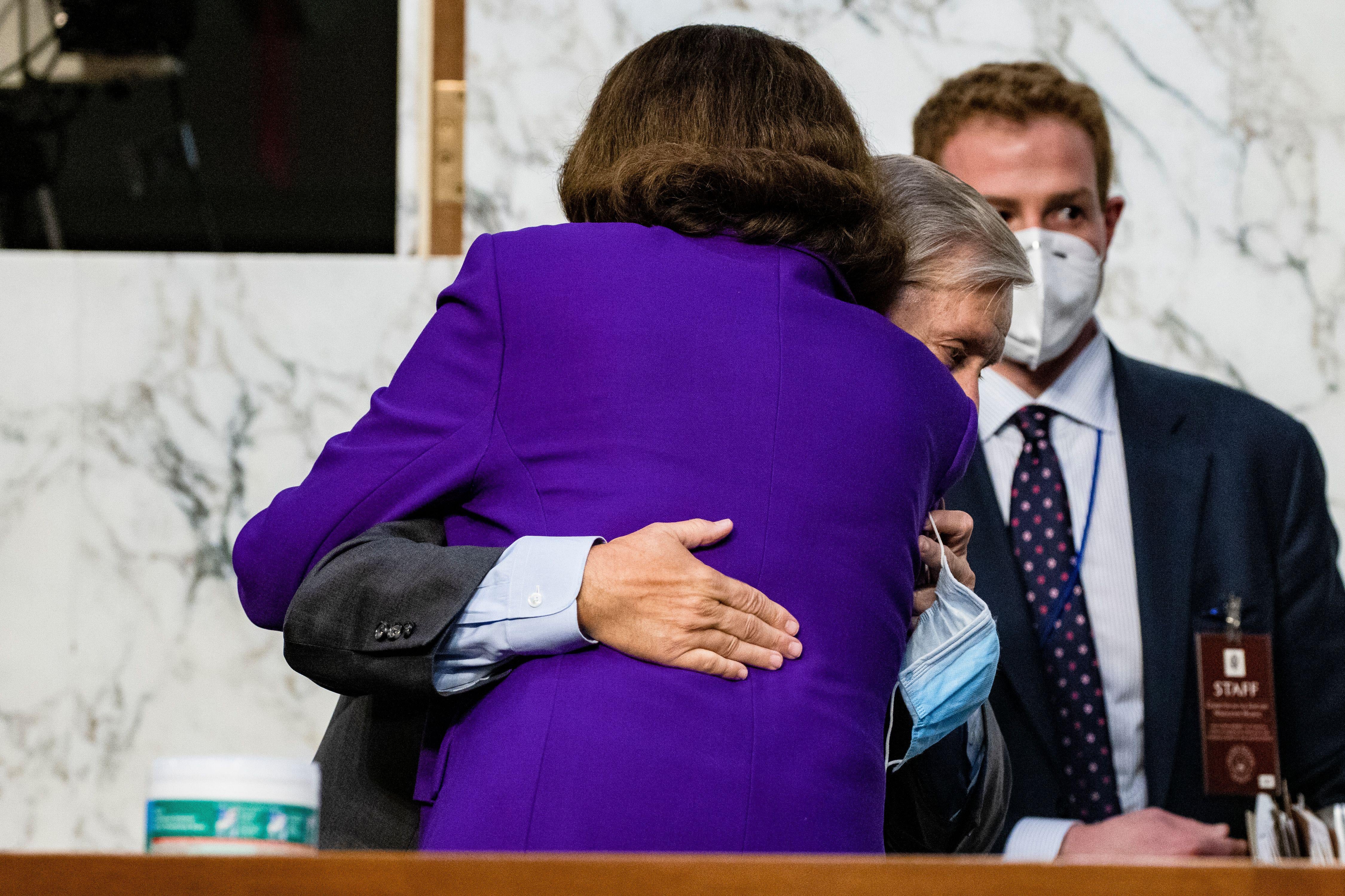 Dianne Feinstein hugs Lindsey Graham, who is holding is mask in his hand.