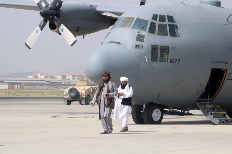 Two Taliban walk in front of a military airplane on the tarmac after U.S. troops withdraw.