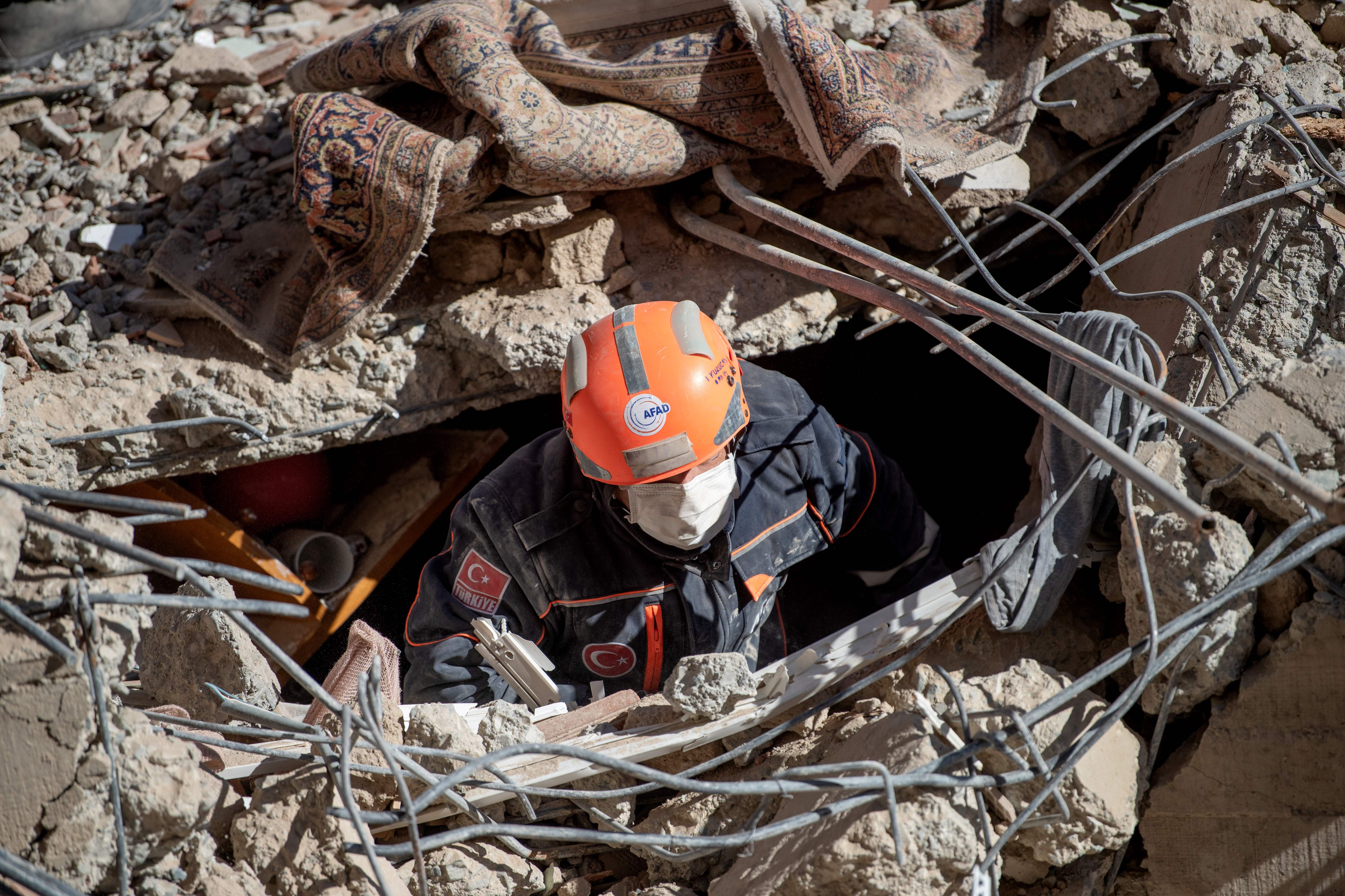 A rescue worker with a mask and hard hat is seen amid the rubble of a collapsed building.