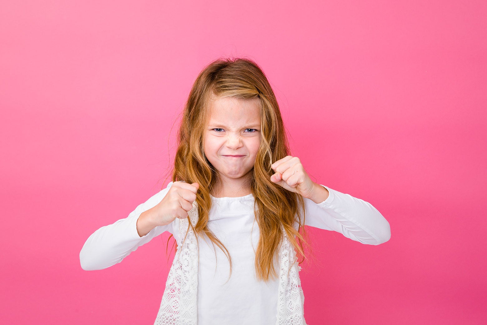 A little girl has a stern expression and puts up her fists, ready to fight.