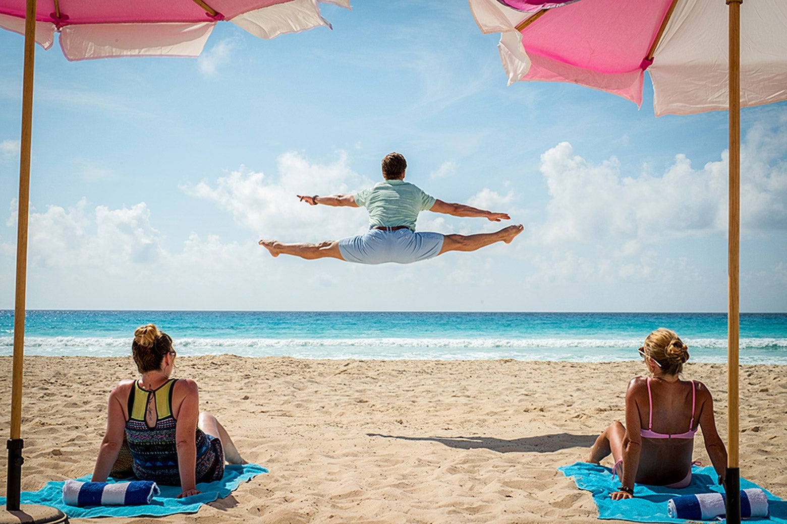 Edgar does a midair split on the beach as two women look on.