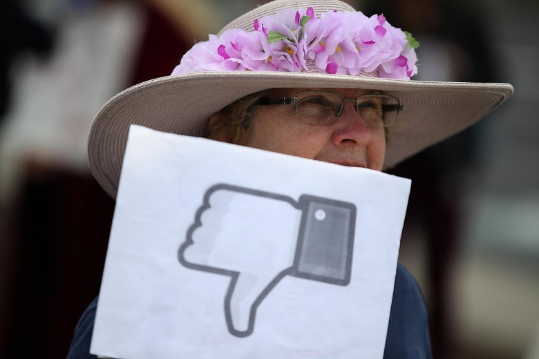 Woman holds a sign with the Facebook thumbs down symbol 