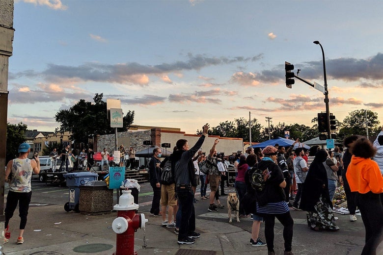 People hold their hands in the air while standing in the middle of an intersection.
