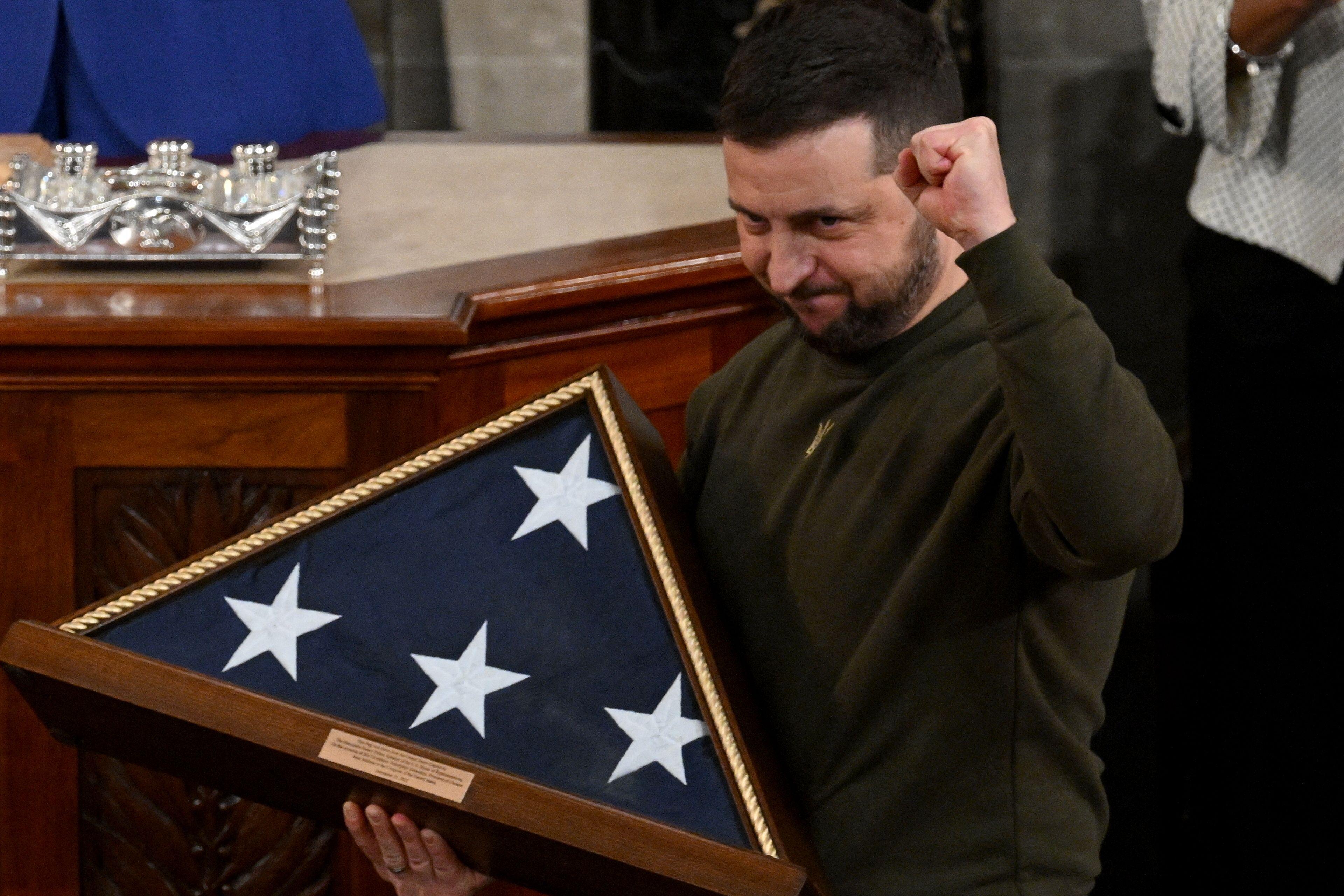 Ukraine's President Volodymyr Zelensky pumps his fist as he holds up a US national flag he received from US House Speaker Nancy Pelosi during a speech in the Congressional chamber.