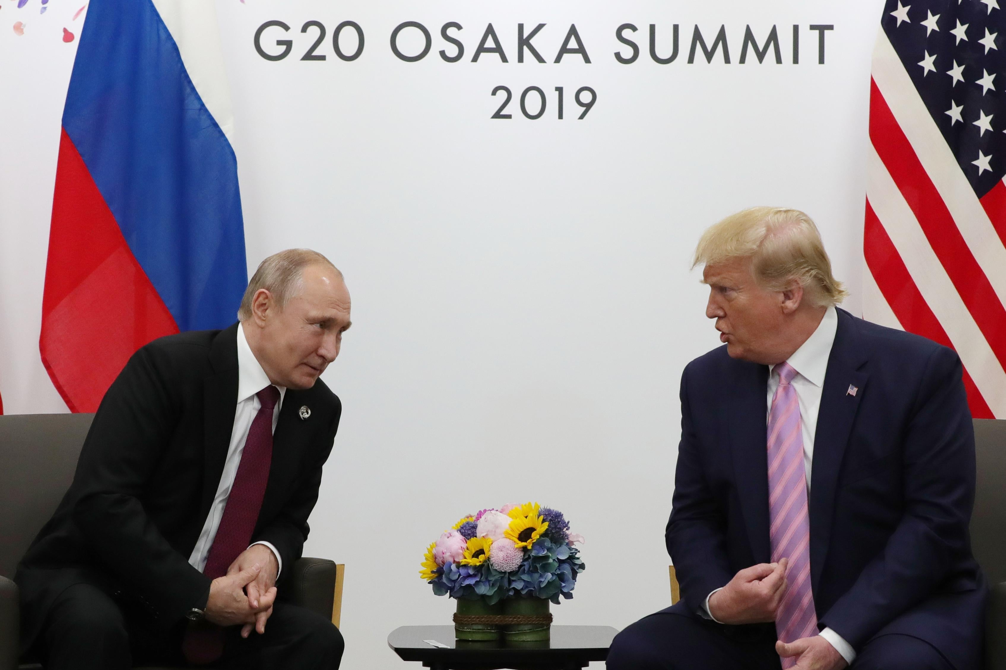 Putin and Trump, seated side-by-side, lean in to speak to one another at a summit.