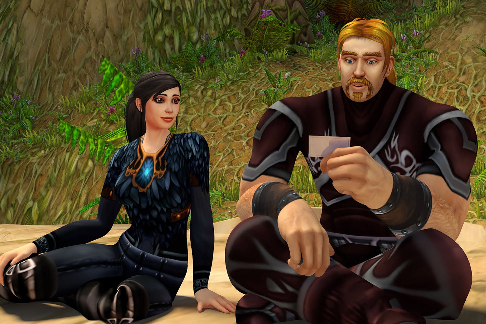 A woman and a man from the game sit next to each other; both are looking at a card the man is holding. 