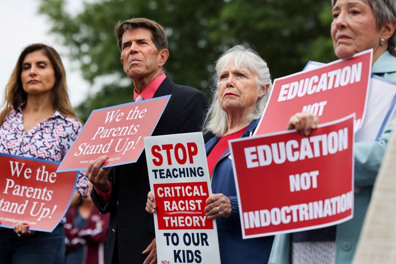 A row of parents holding up signs that say "Education Not Indoctrination," "Stop Teaching Critical Racist Theory to Our Kids," and "We the Parents Stand Up!"