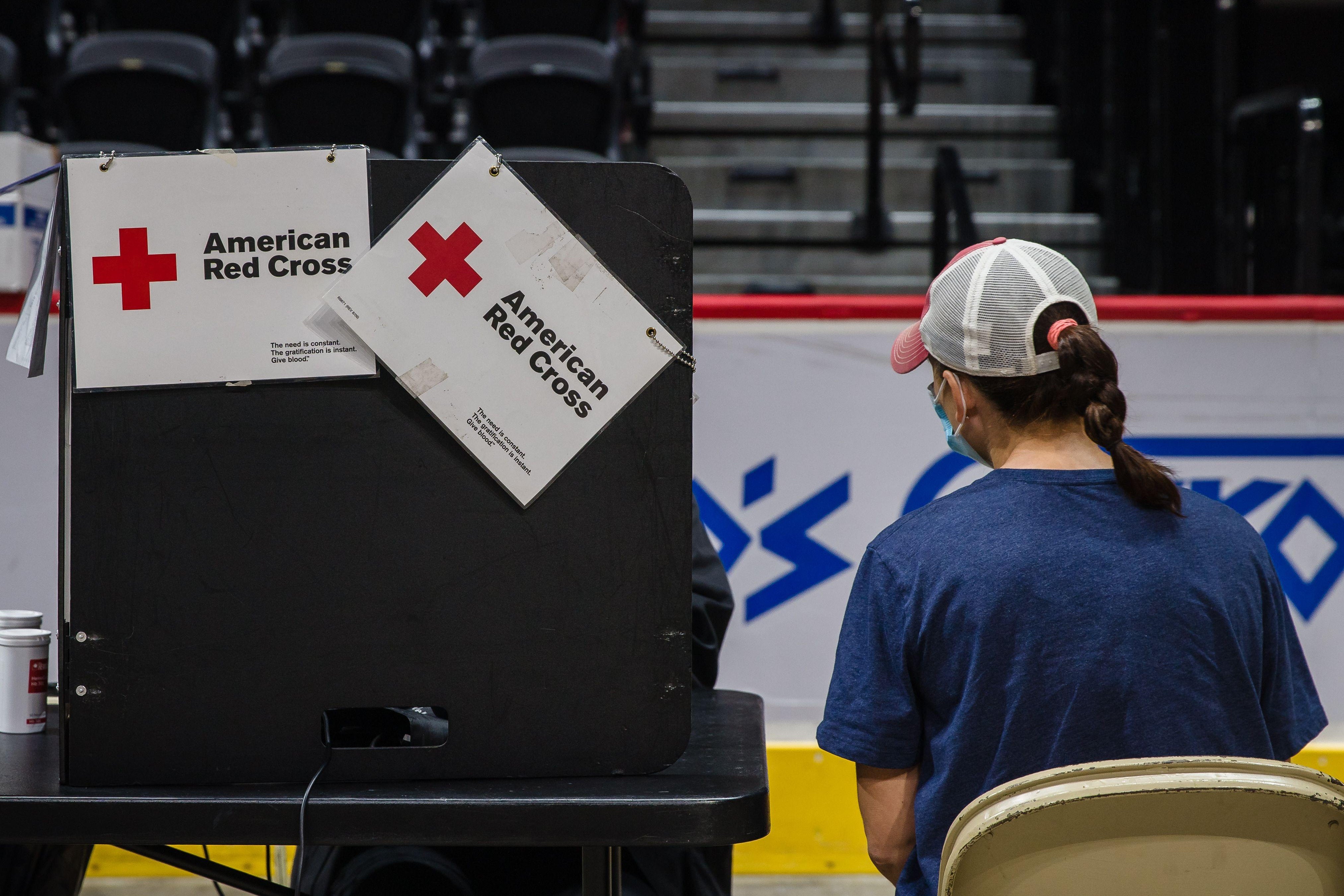 A woman interviews who is about to donate blood sits next to a privacy divider that has the American Red Cross logo on it