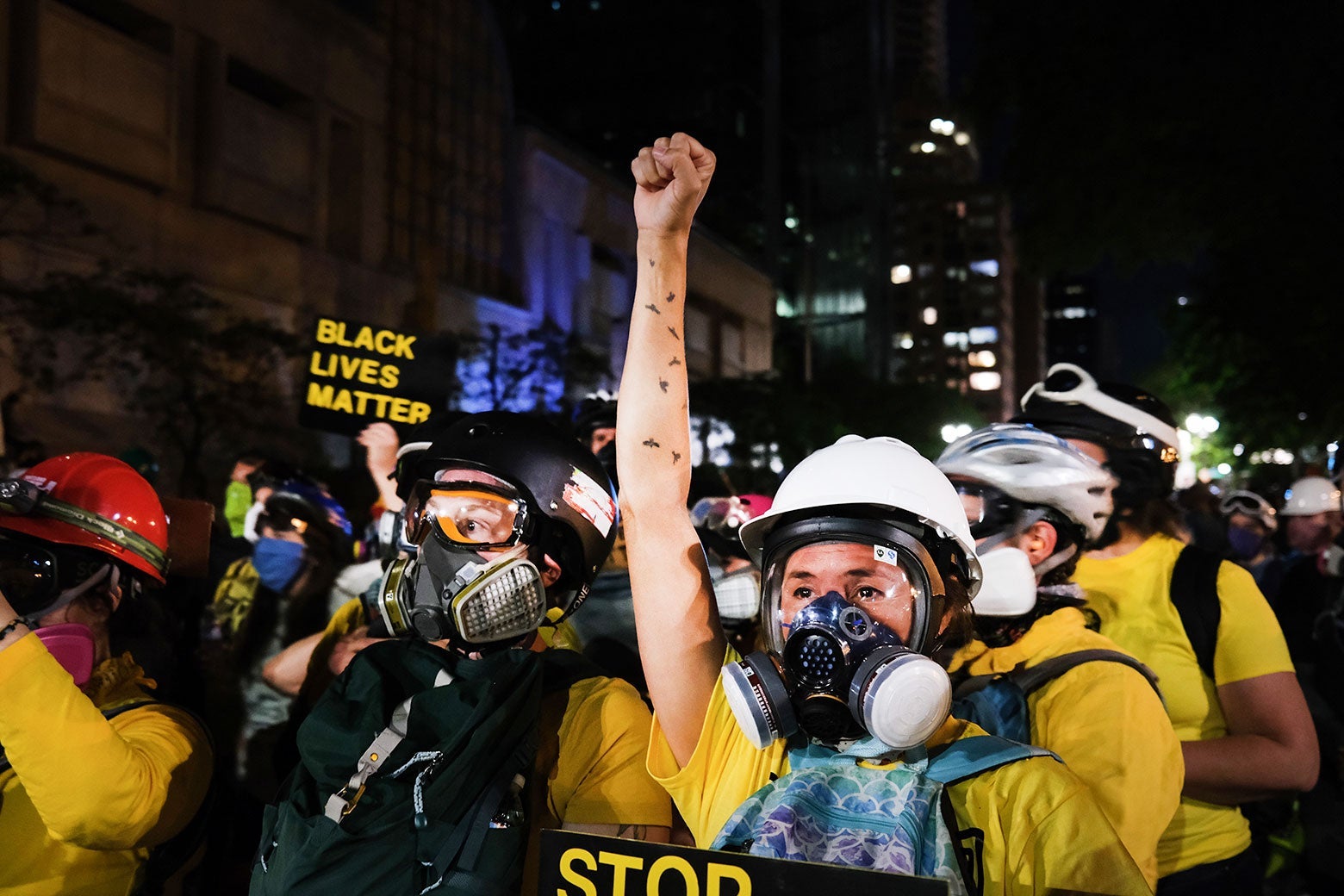 A protester wearing a mask and helmet holds up a fist amid a crowd of others.
