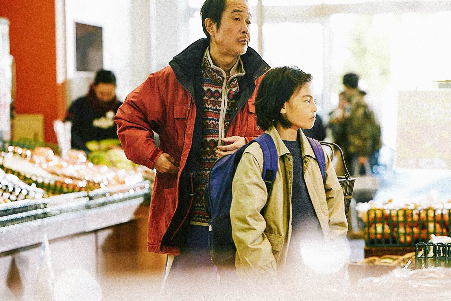 A still from Shoplifters depicts characters Osamu (Lily Franky) and Shota (Jyo Kairi) standing at a grocery store.