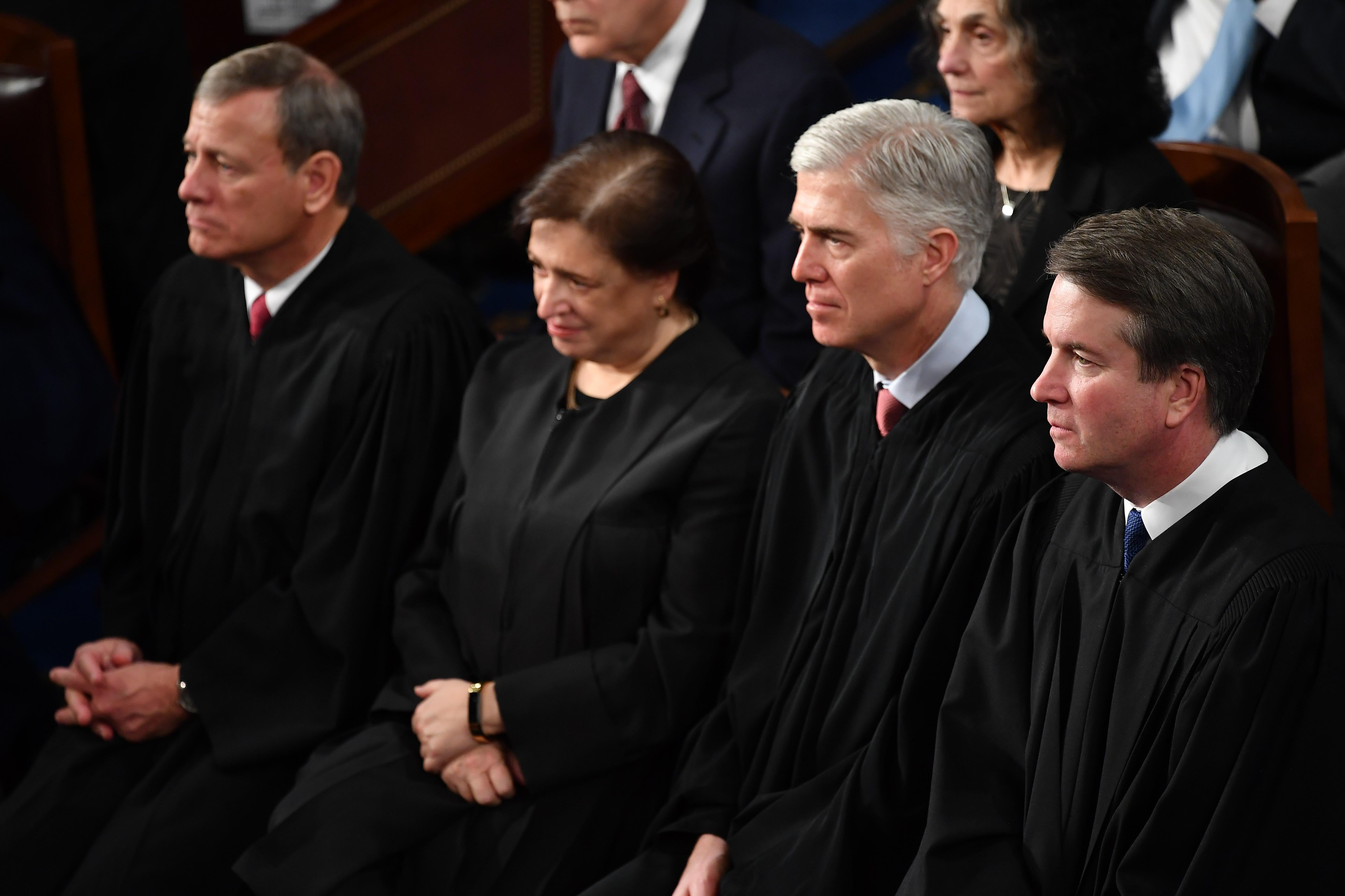 Four Supreme Justices in their justice robes listening intently.