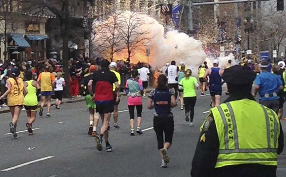Runners continue to run towards the finish line of the Boston Marathon as an explosion erupts near the finish line.
