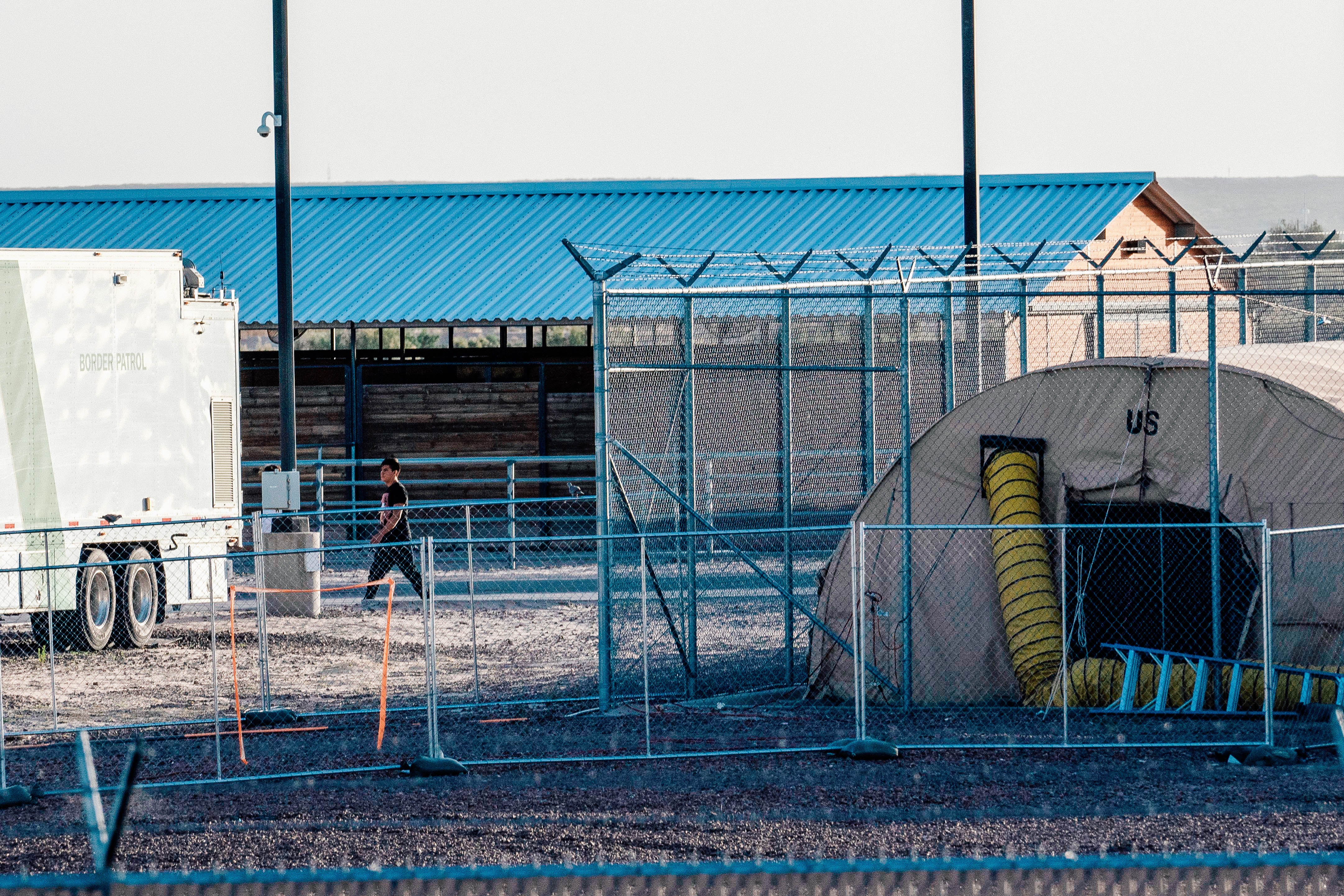 A tent and barrack behind barbed wire fencing.