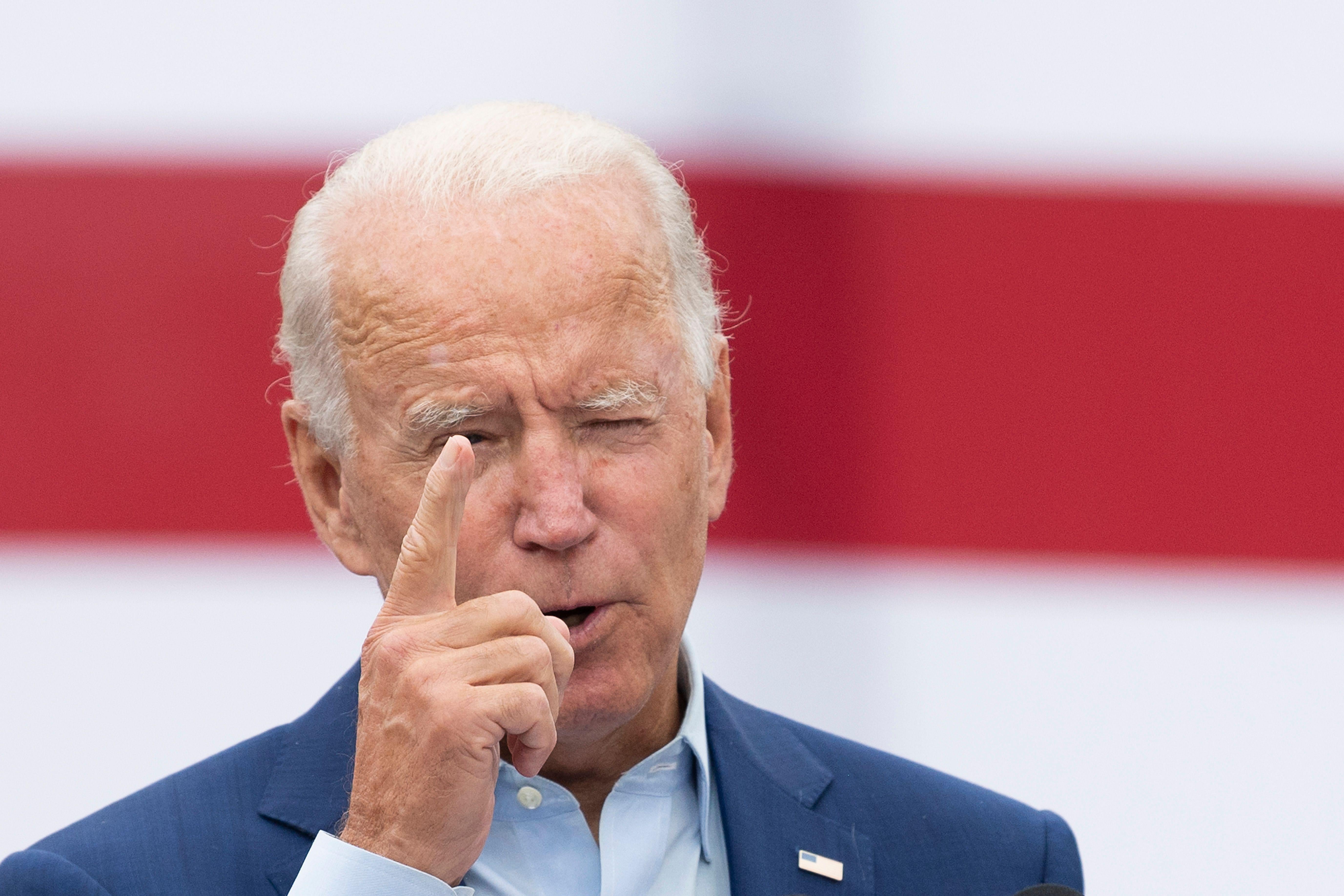 Joe Biden holds up a finger as he speaks in front of an American flag
