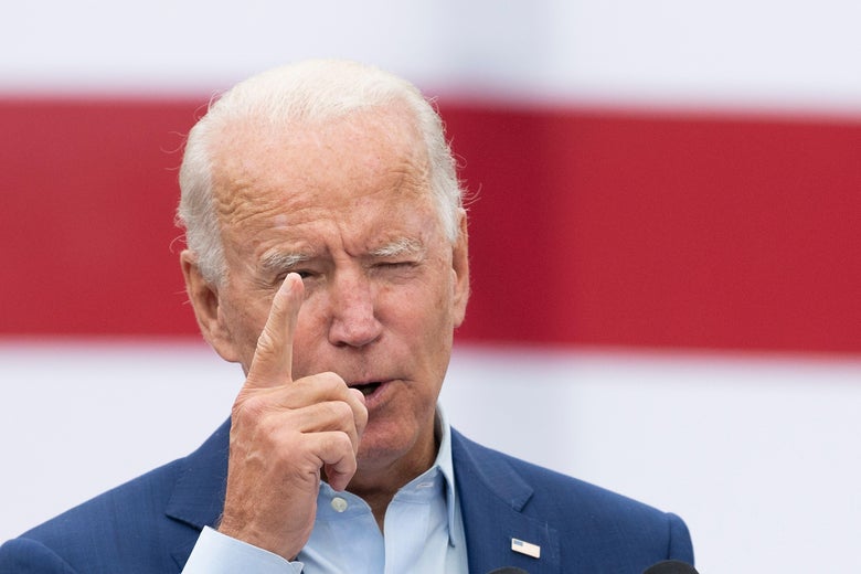 Joe Biden holds up a finger as he speaks in front of an American flag